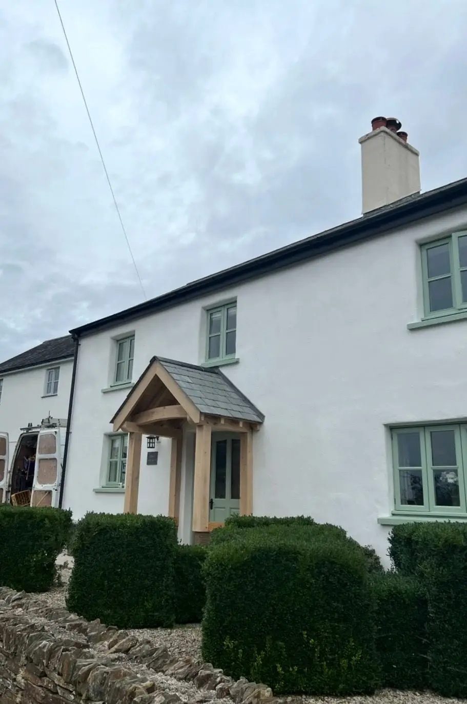 White rendered cottage with green windows and a new oak porch
