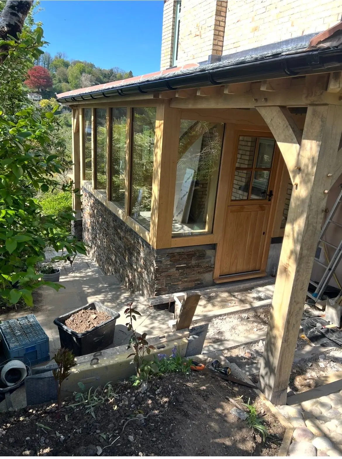 Oak framed extension with a stone plinth and glazed panels, part way through the build