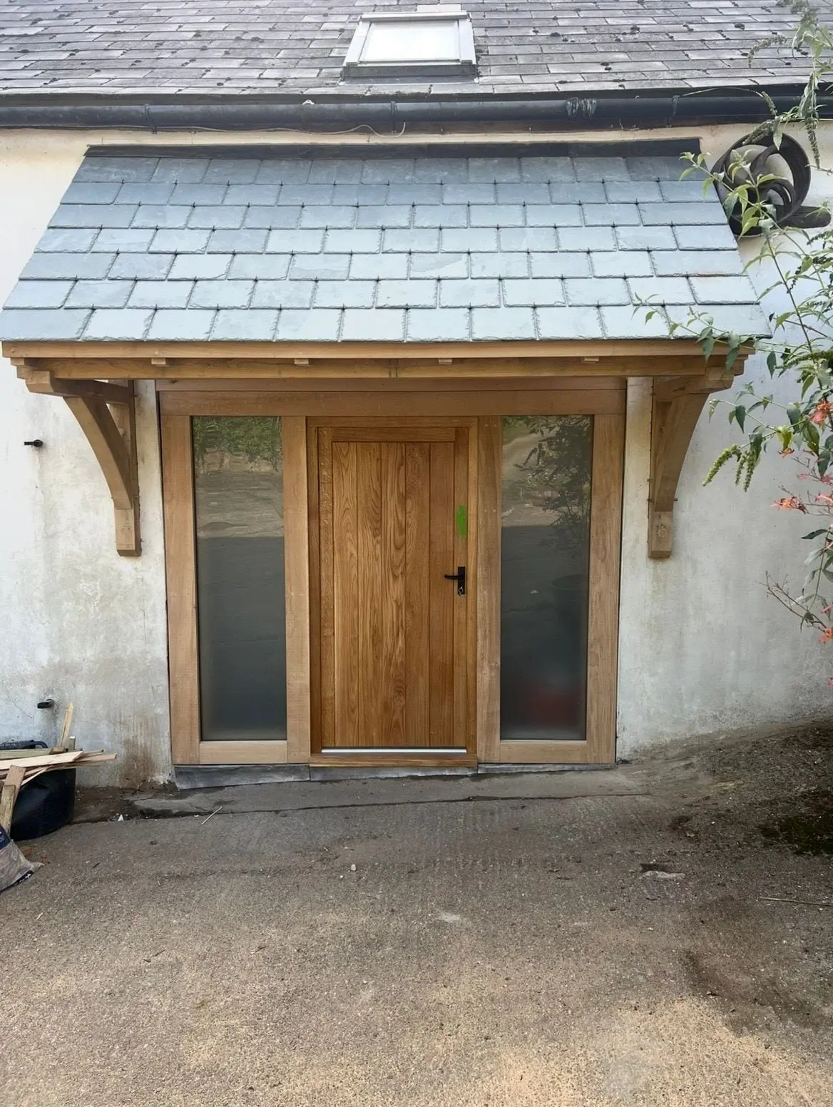 Oak front door with glazed side panels under a slate roofed oak porch