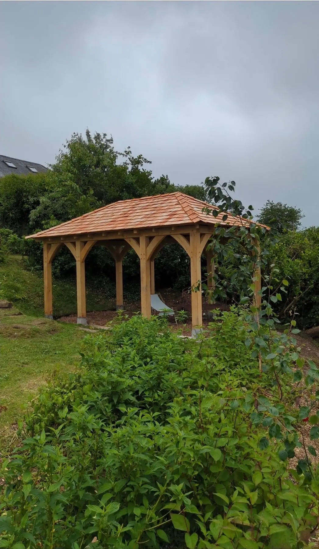 Oak gazebo in a garden with shrubs around it