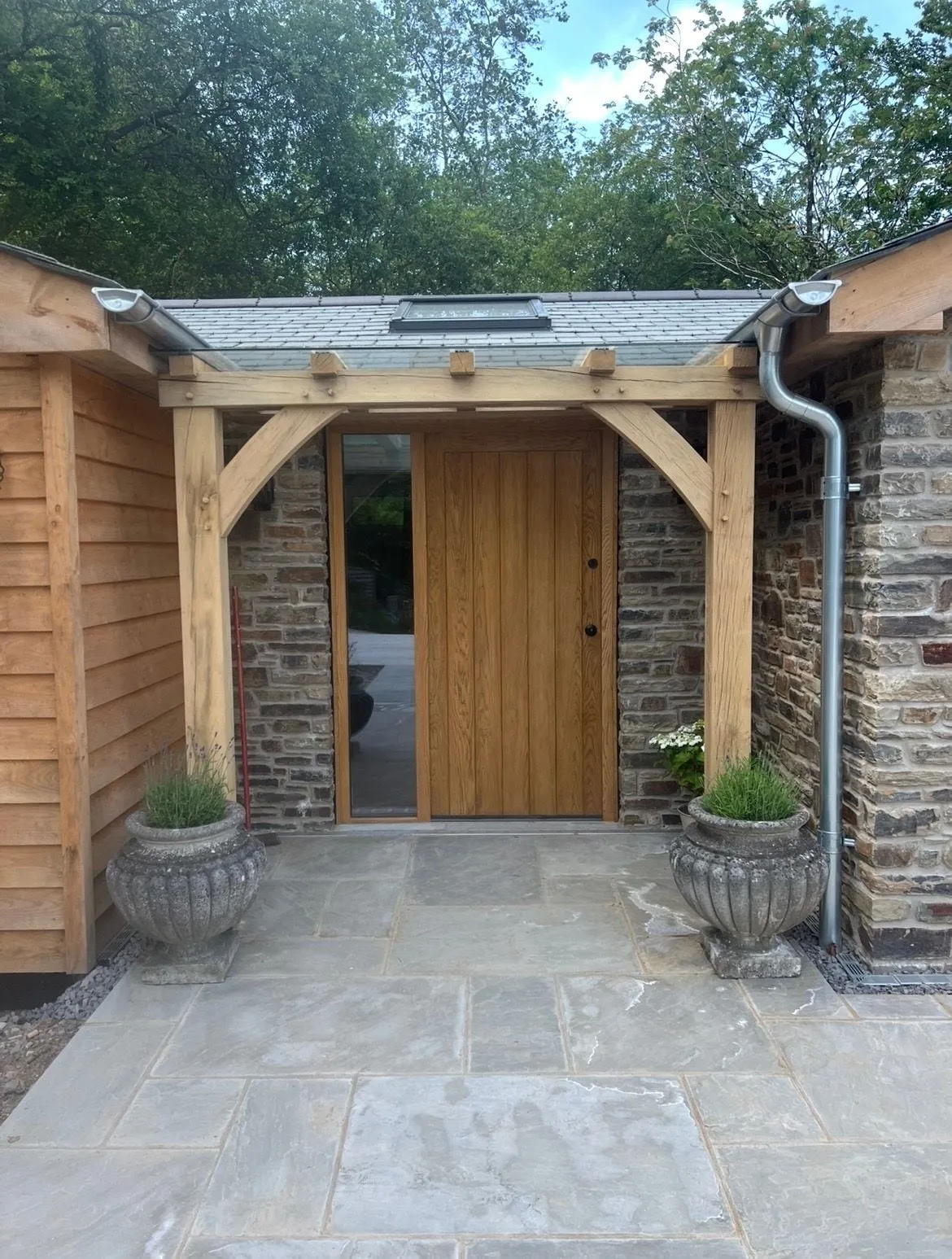 Oak framed porch with curved braces and an oak front door on a stone and timber clad house