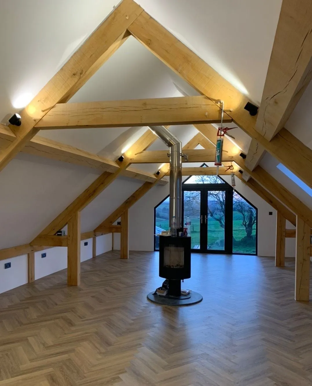 Finished attic room with exposed oak trusses, a herringbone floor and a wood burning stove