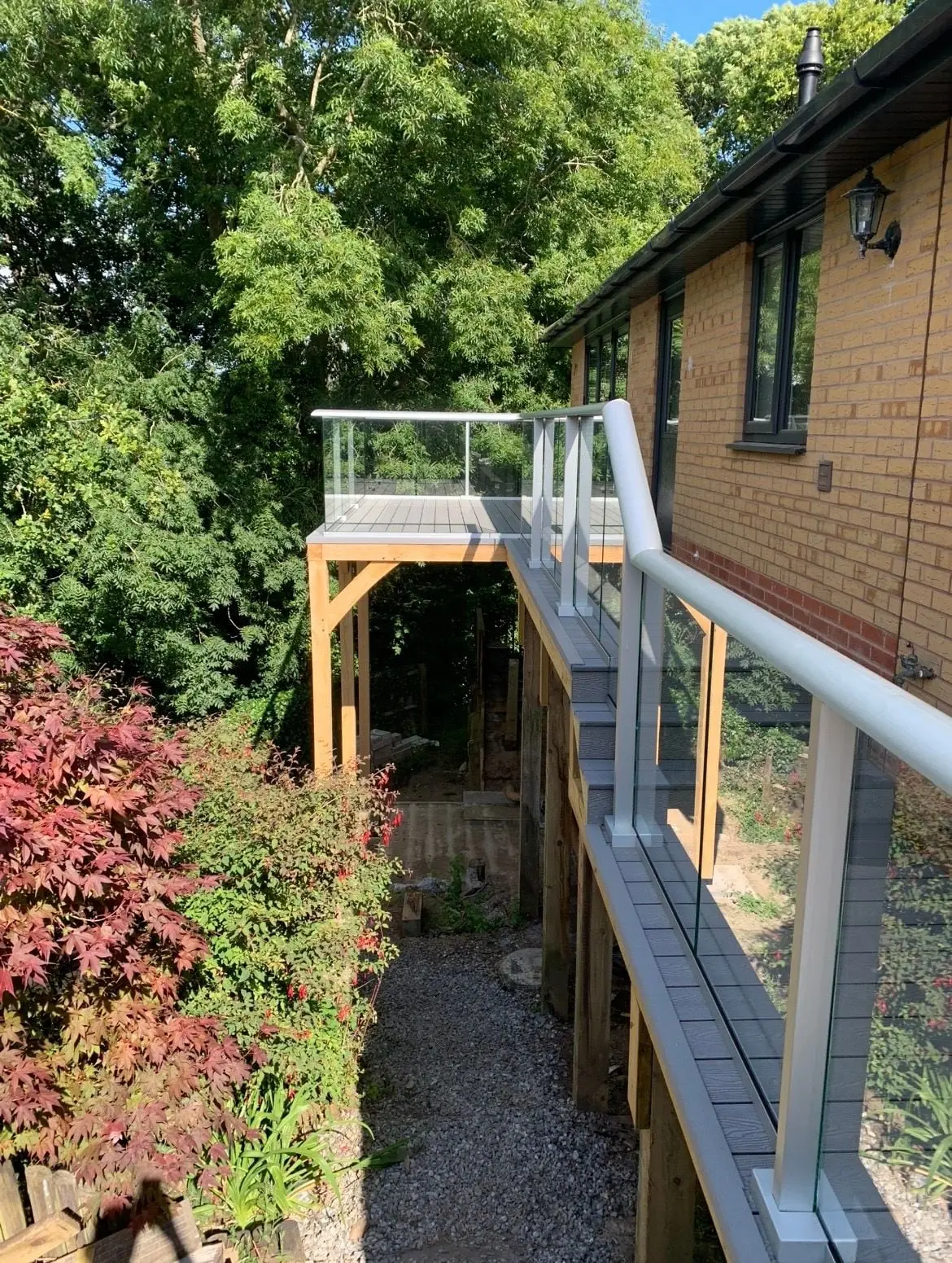 Raised deck beside a brick house, with a glass balustrade and the garden below