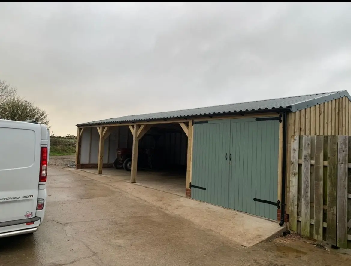 Timber framed cart shed with an open front and sage green double doors