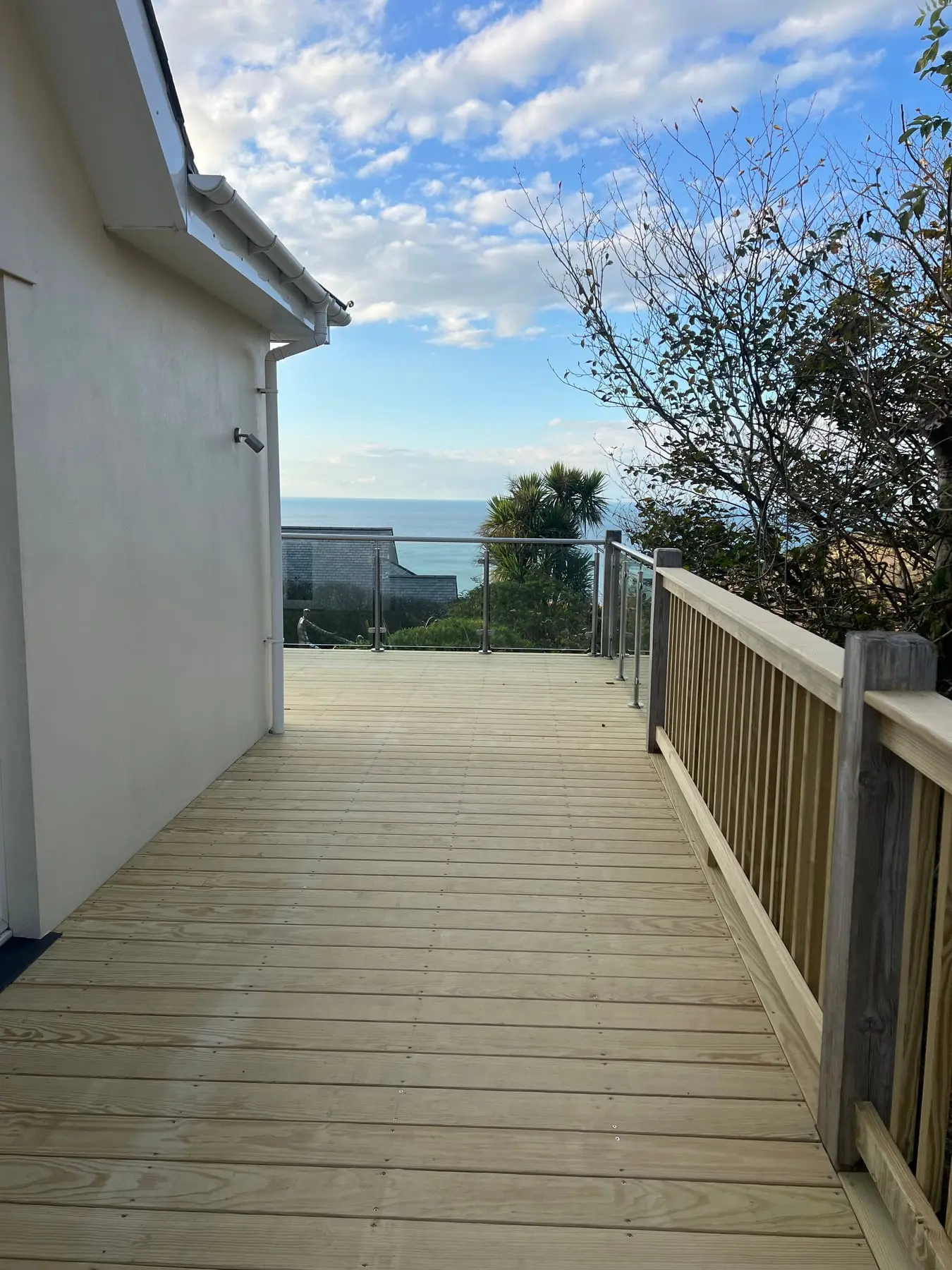 New timber decking beside a house, with a timber balustrade and glass panels looking out to sea